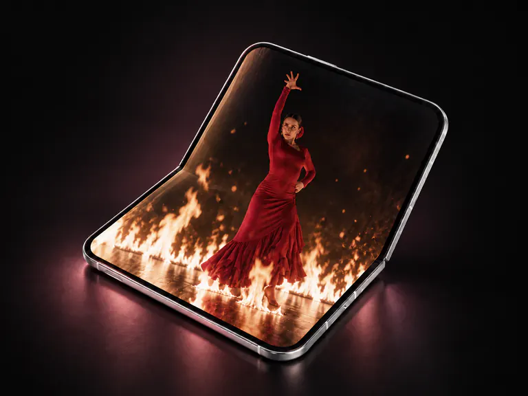 A half-folded iPhone Duo showing a cinematic scene of a red-dressed dancer amid firelight